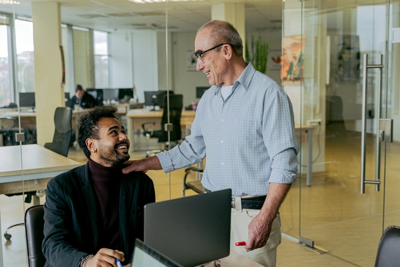 older-man-smiling-and-touching-shoulder-of-younger-coworker-at-office-job-vs-career